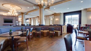 Un moderno vestíbulo de hotel con área de bar, disposición de asientos y una gran araña.