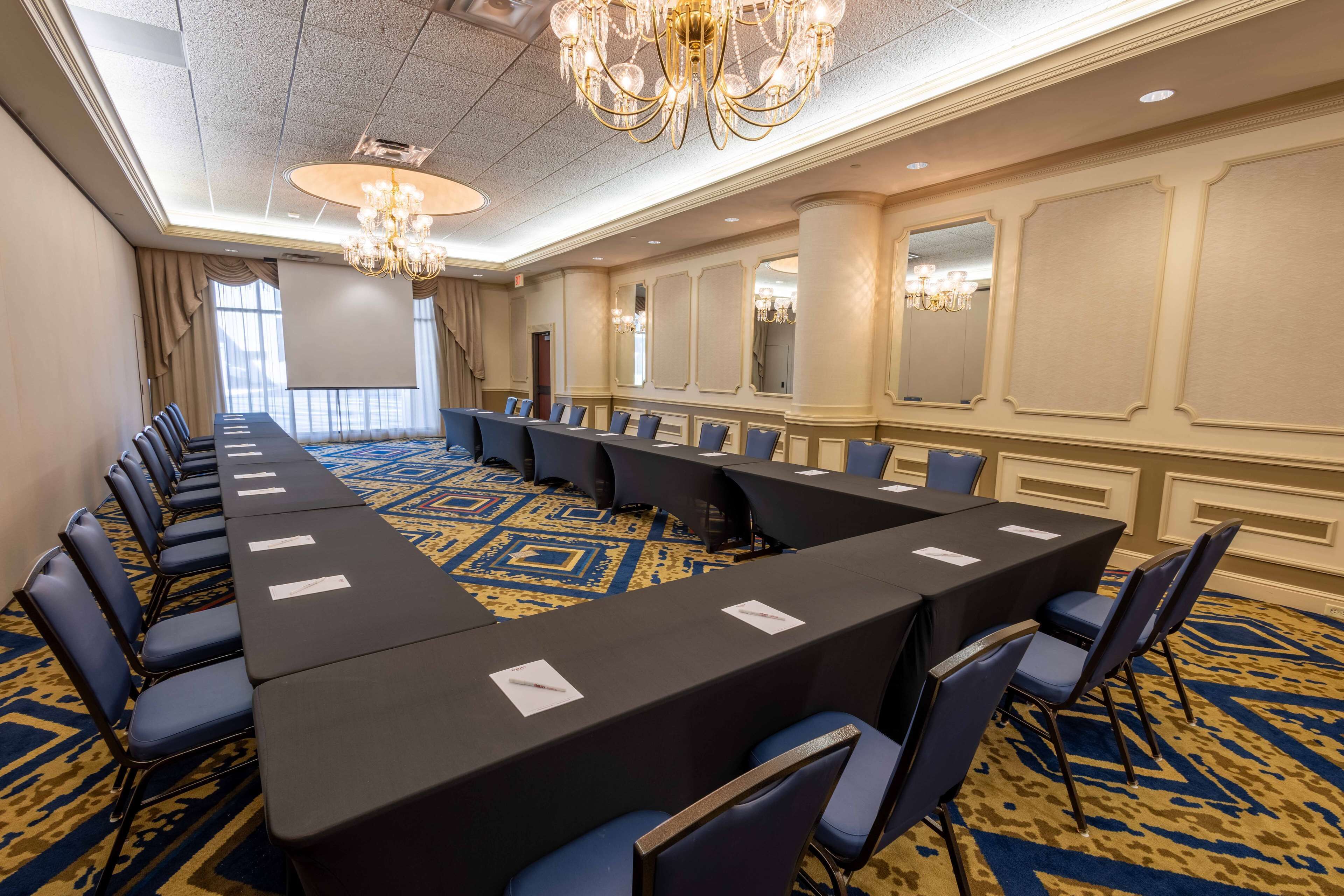 Une salle de conférence avec une longue table, des chaises bleues et un tapis à motifs.