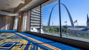 Habitación de hotel con un ventanal grande que ofrece vistas al Gateway Arch y a un edificio moderno.
