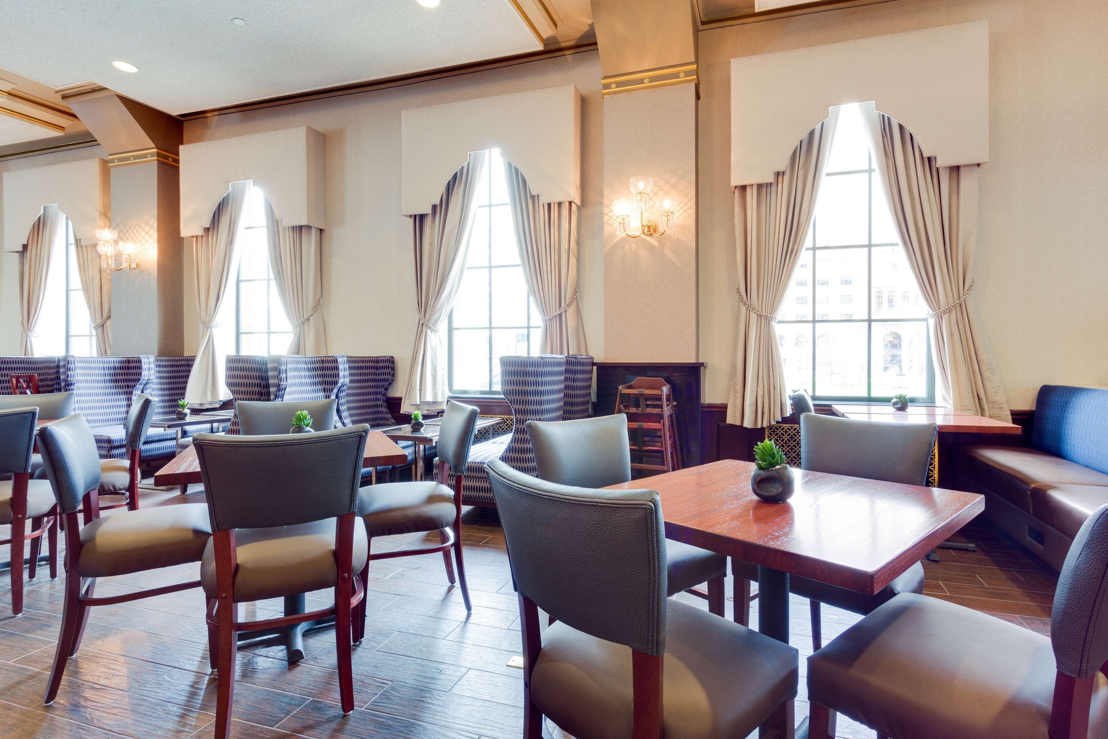 A restaurant with booths and tables, large windows with curtains, and a chandelier.