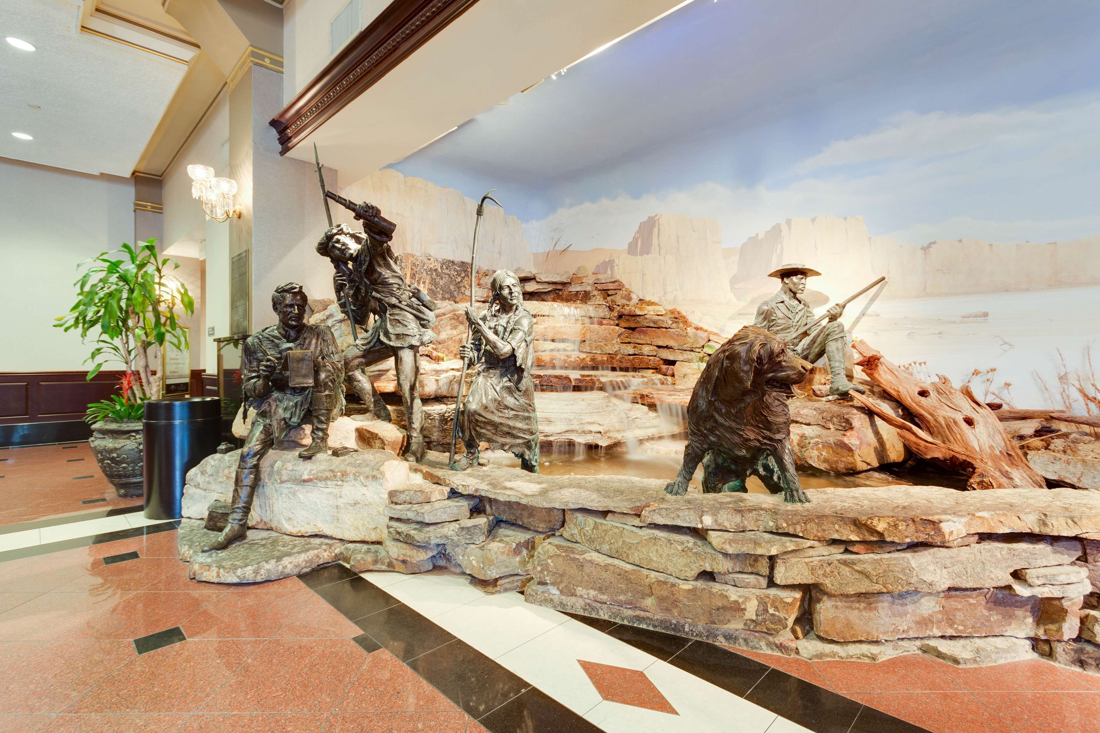 A lobby with a large sculpture of historical figures, a chandelier, and a plant.