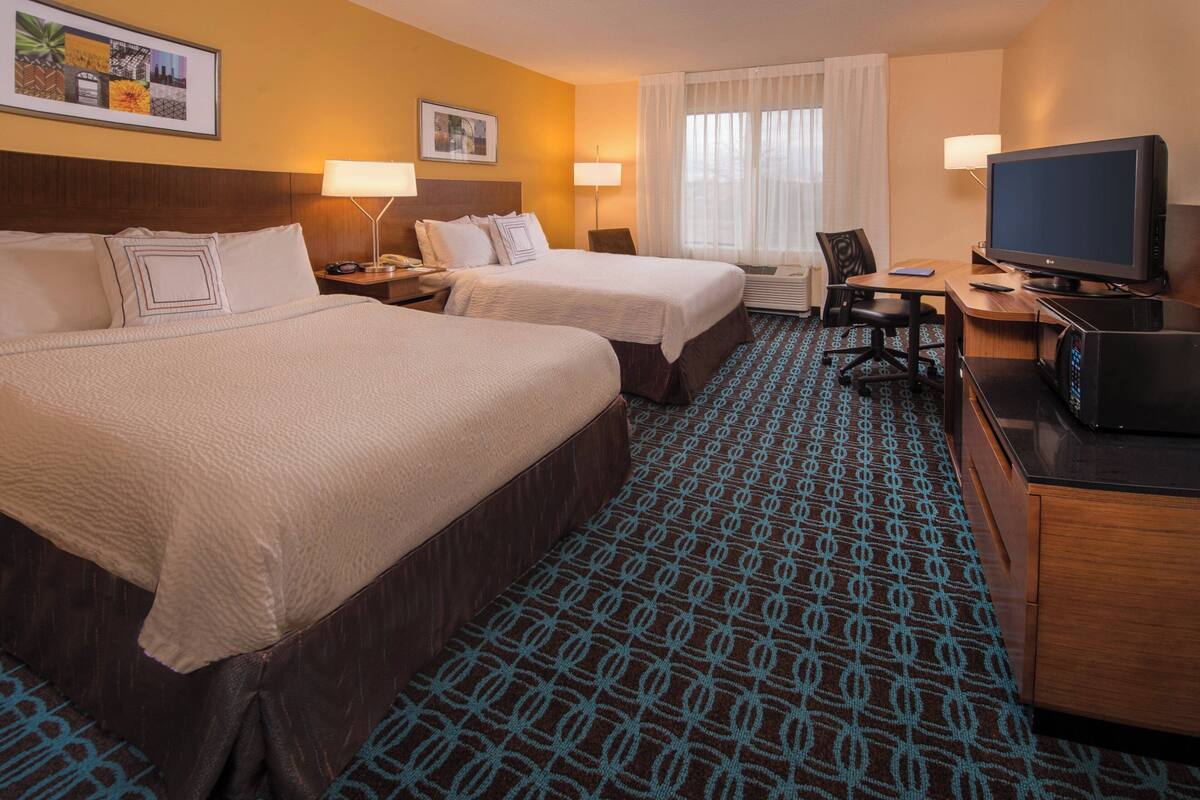 A hotel room with two beds, a desk with a television, and a patterned carpet.