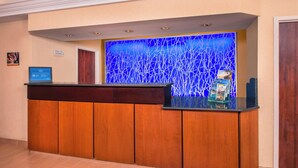 A reception desk with a blue abstract wall design, a wooden counter, and a sign indicating the location. - Fairfield Inn & Suites Dulles Airport Chantilly (Chantilly)