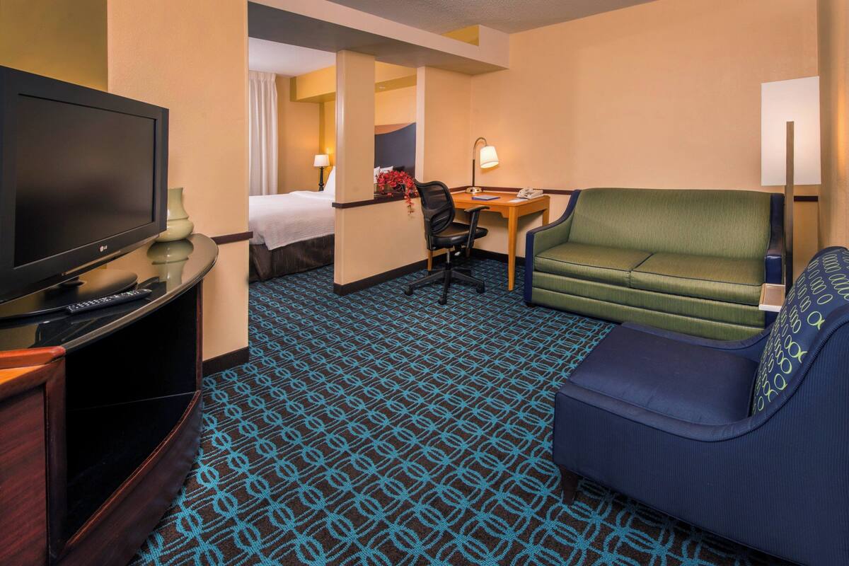 A hotel room with a TV, a desk, a green sofa, and a bed.