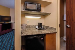 Una kitchenette compacta con microondas, cafetera y refrigerador pequeño.