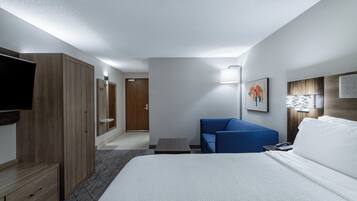 A hotel room with a large bed, a blue sofa, a TV, a desk, and a wardrobe.