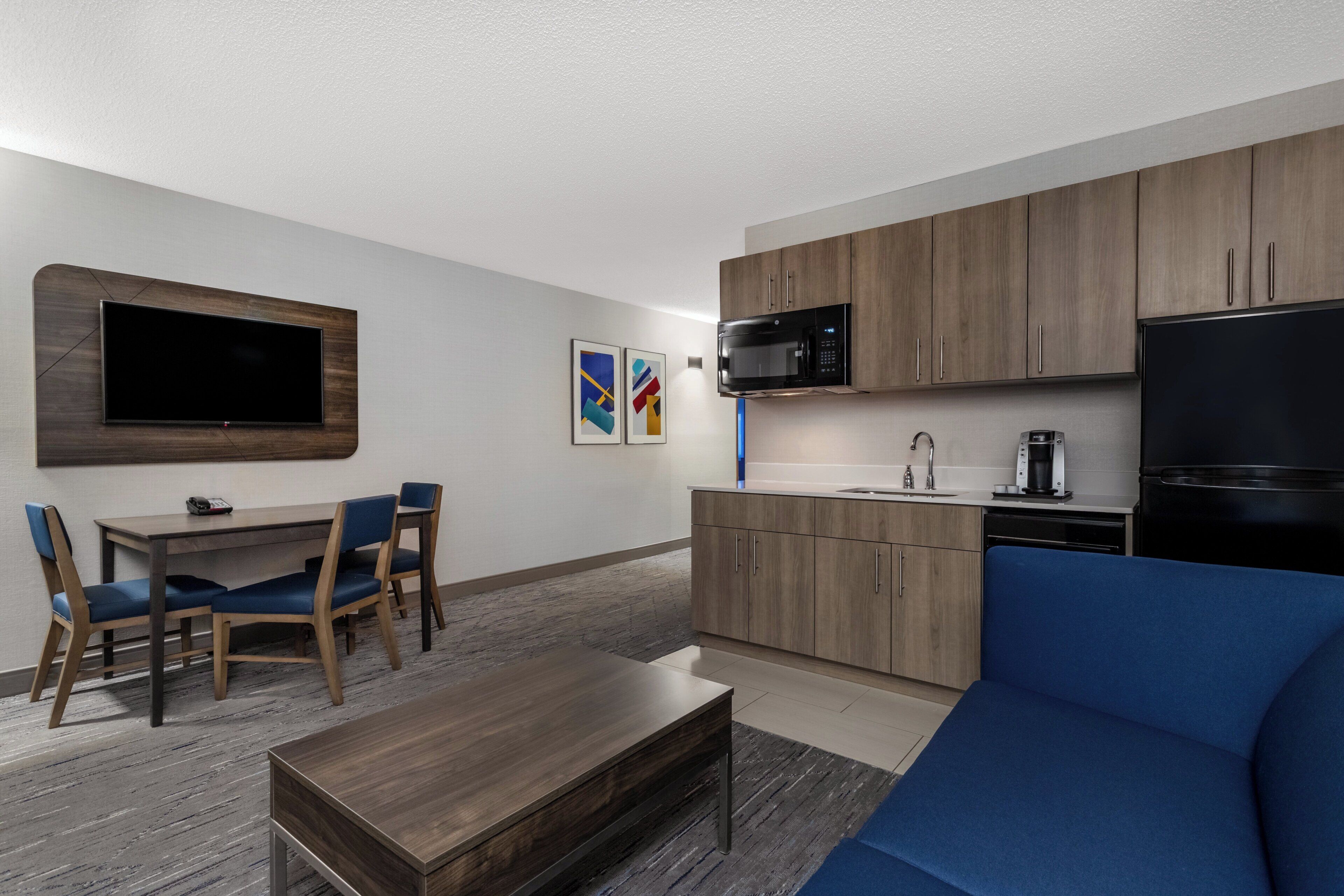 Una sala moderna con un televisor de pantalla plana, un comedor con mesa y sillas, y una cocina con microondas y refrigerador.