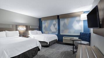 Habitación de hotel con dos camas, un televisor de pantalla plana, una mesita, una silla y una ventana con cortinas de diseño geométrico.