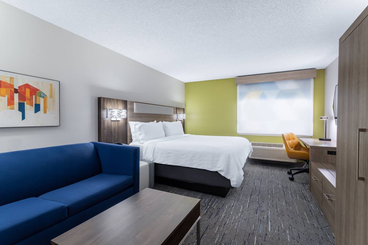 A hotel room with a bed, a blue sofa, a desk, and a window with a view.