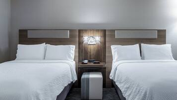 Une chambre d’hôtel avec deux lits, une table de chevet, une lampe fixée au mur et un petit pouf.