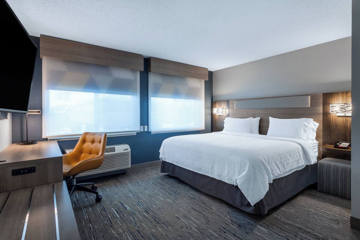 A modern hotel room with a large bed, a desk, and a chair.
