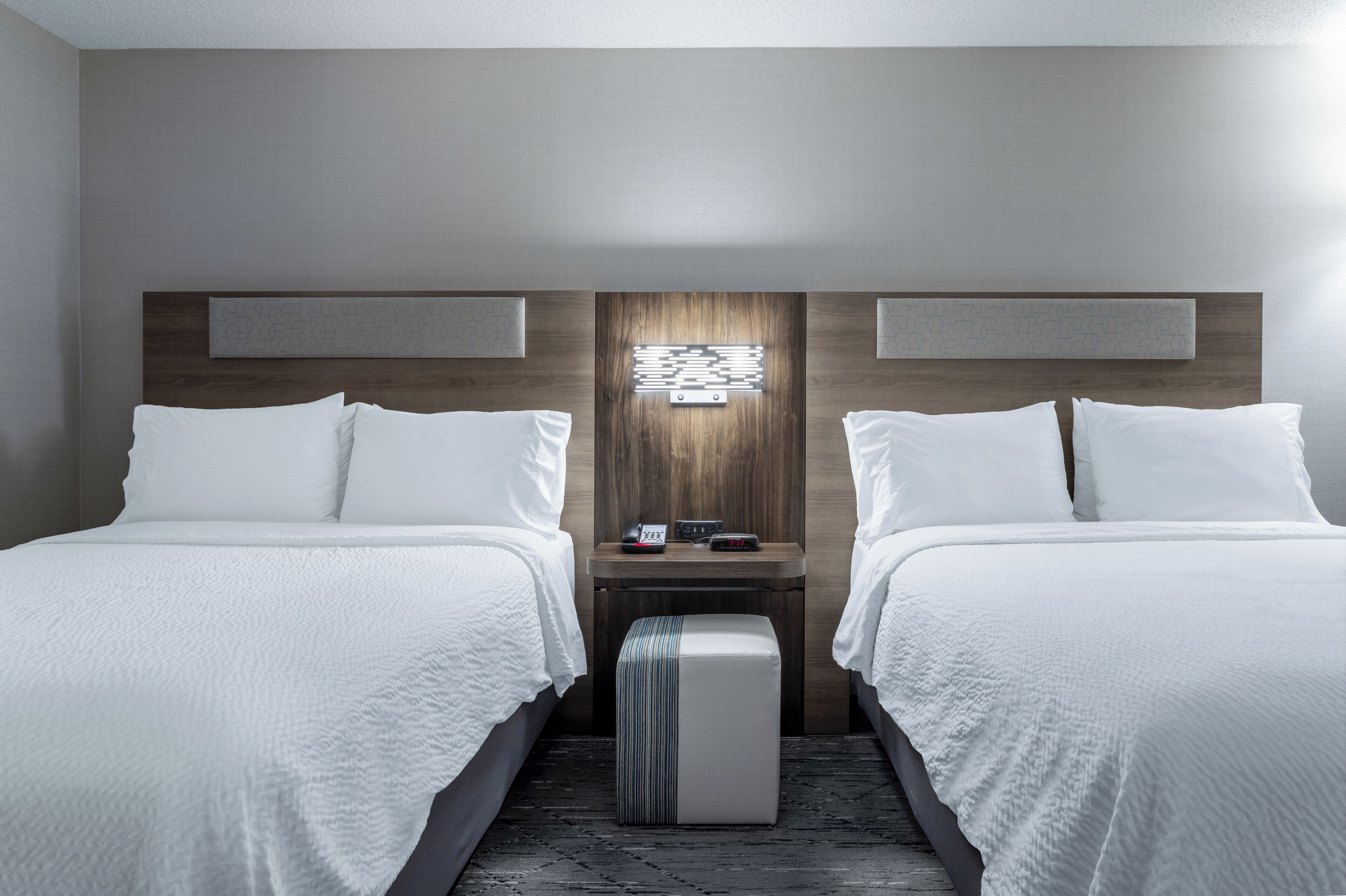 A hotel room with two beds, a nightstand, and a wall-mounted light fixture.
