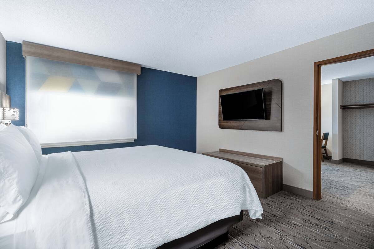 A hotel room with a bed, a TV mounted on the wall, and a wooden bench.