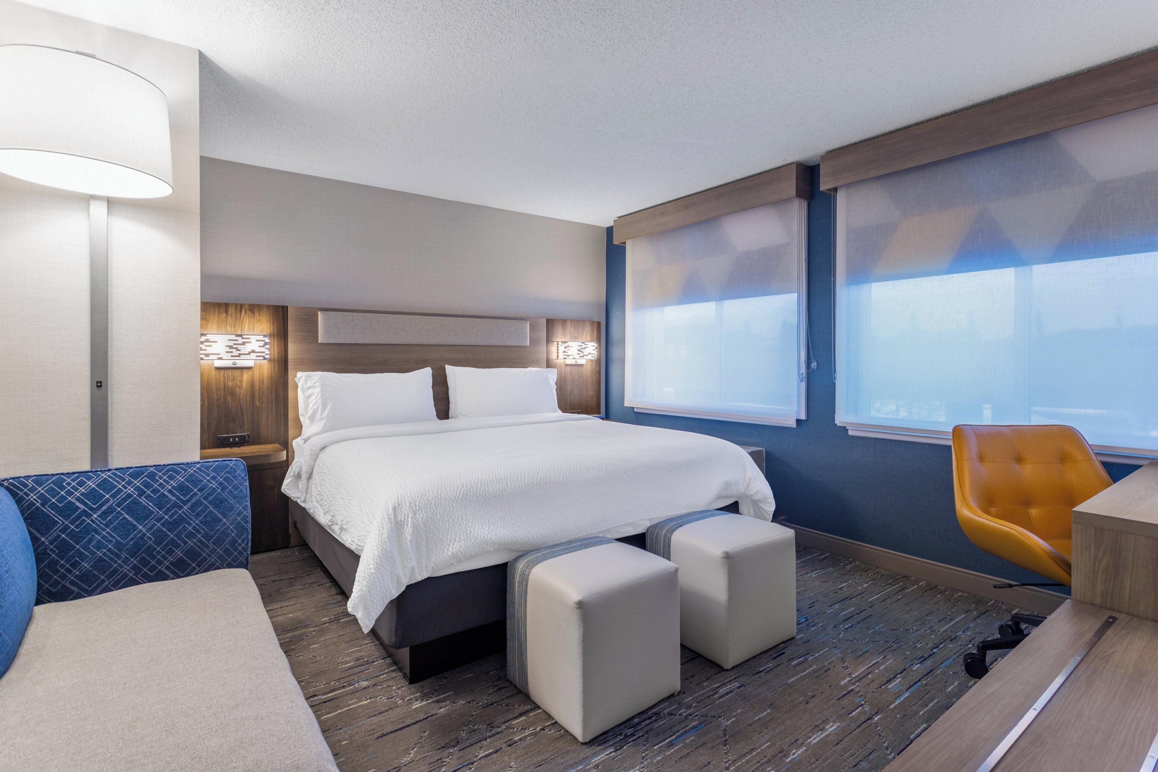 A hotel room with a bed, a desk, a chair, and a window.
