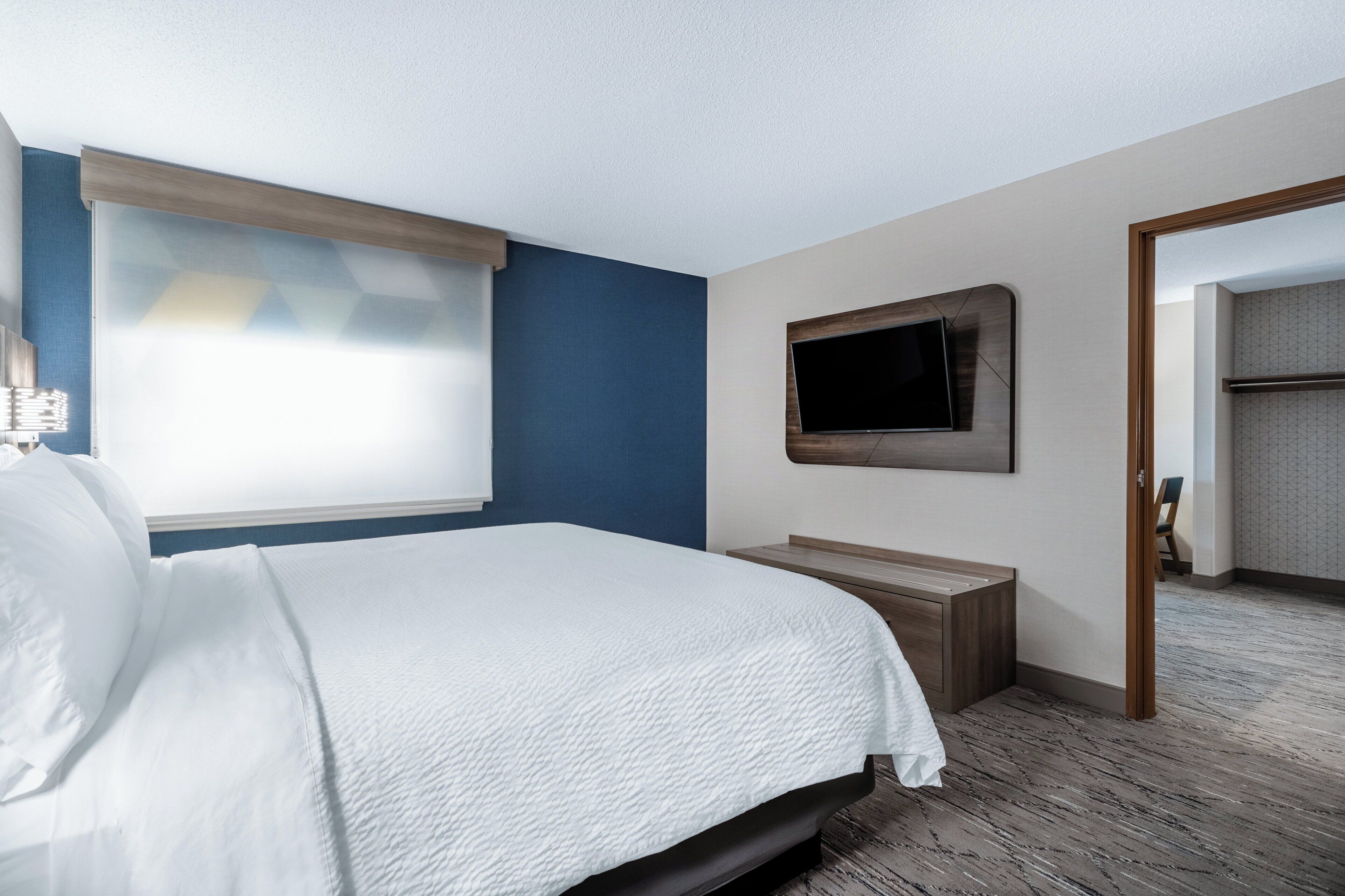 Una habitación de hotel con una cama, un televisor montado en la pared y un banco de madera.