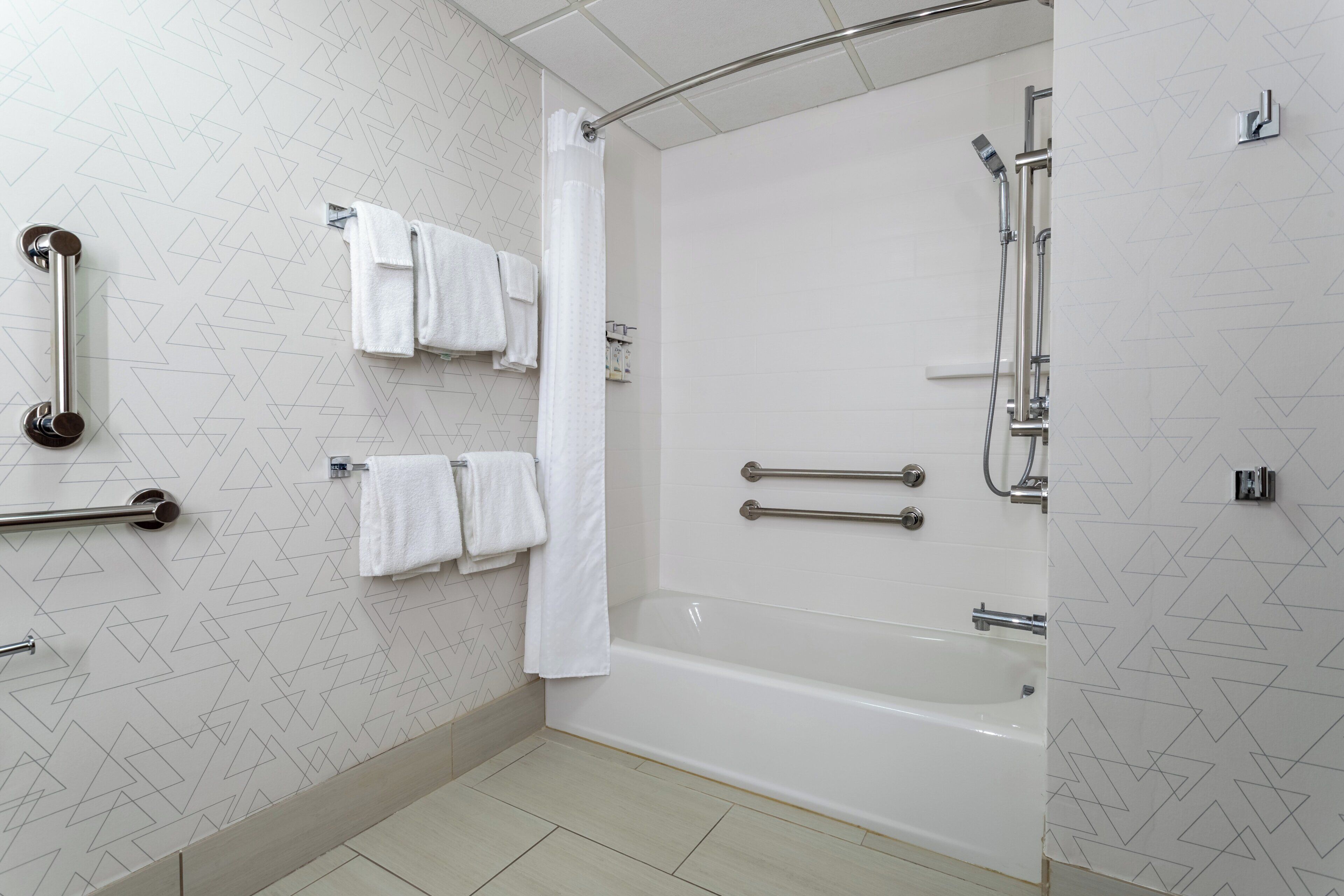 A modern bathroom with a bathtub, handrails, and a shower area.