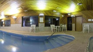 An indoor swimming pool with wooden walls and ceiling, surrounded by white chairs and a table. - Holiday Inn Express & Suites Wauseon by IHG (Wauseon)
