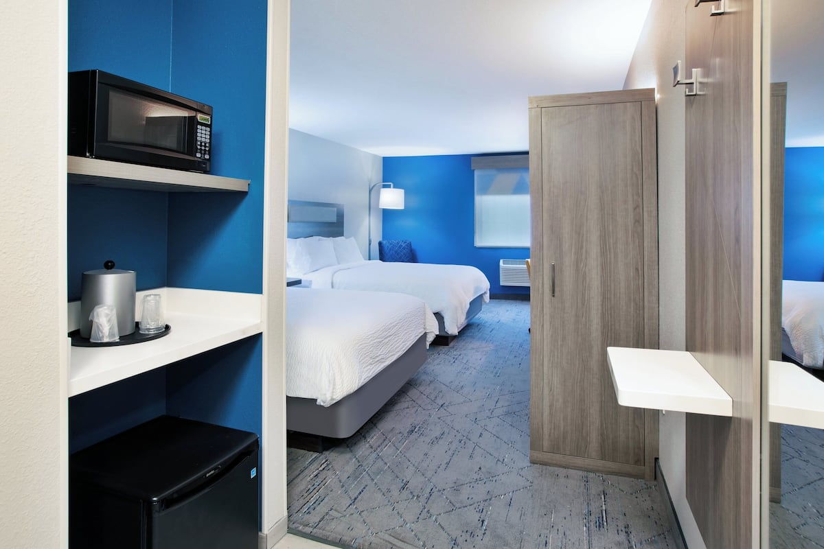A hotel room with two beds, a microwave, a mini fridge, a bedside table, and a wardrobe.