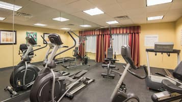 Un gimnasio con equipo de ejercicio, espejos y un cartel que indica la ubicación.