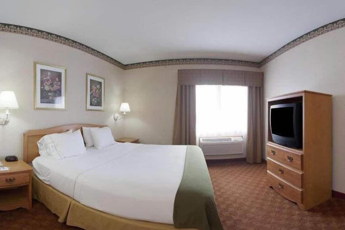 A hotel room with a large bed, bedside lamps, a television, and a window with curtains.