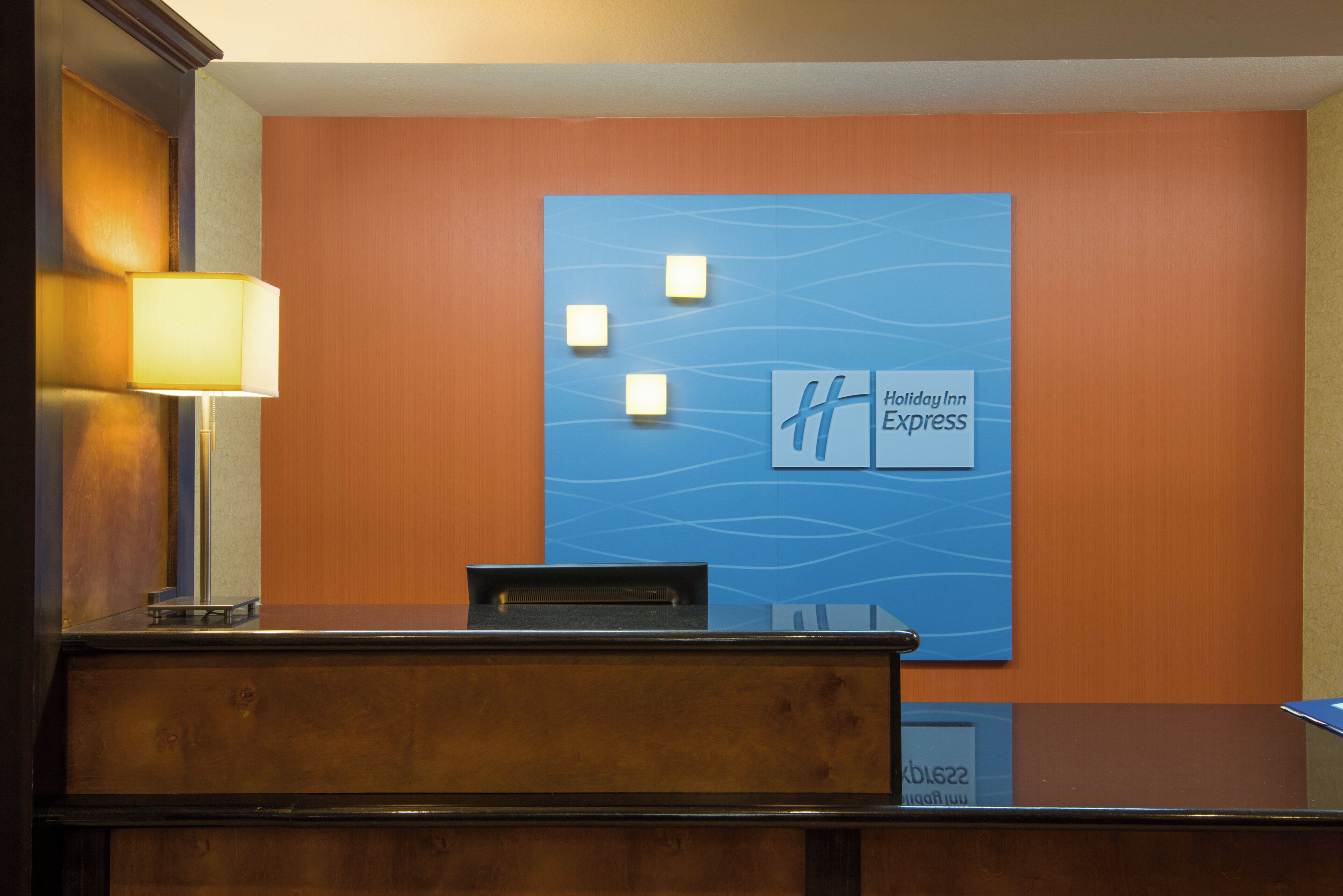 Ein Empfangsschalter mit blauer Wand, mit dem Holiday Inn Express Logo und drei beleuchteten Schildern.