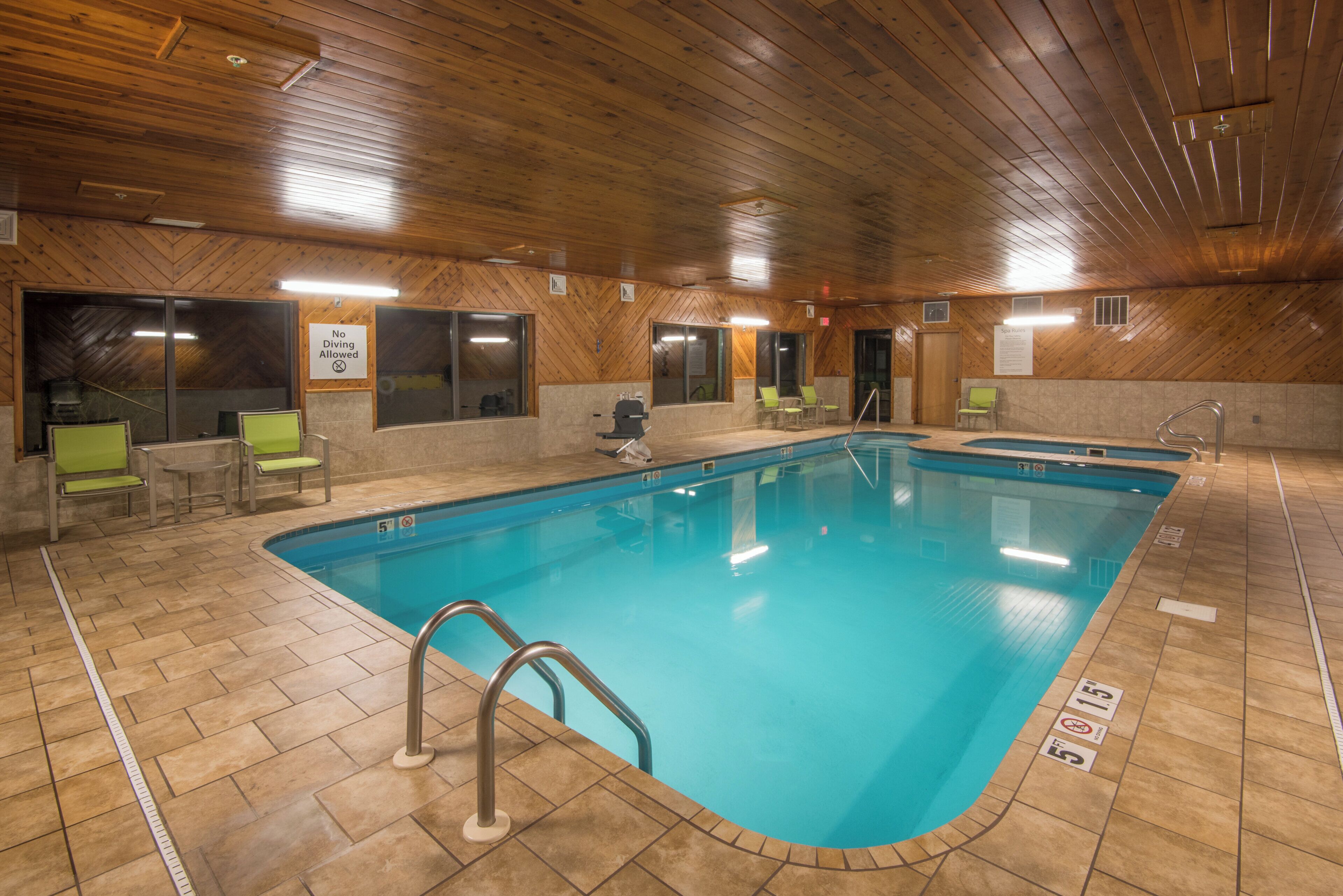 An indoor swimming pool with clear water, surrounded by tiled flooring and wooden walls.