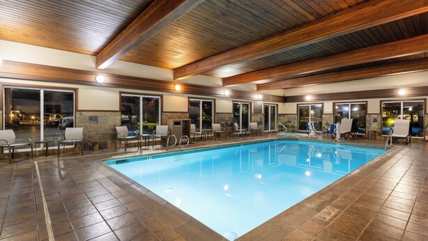 An indoor swimming pool with tiled flooring, wooden ceiling beams, and multiple seating areas with chairs and tables.