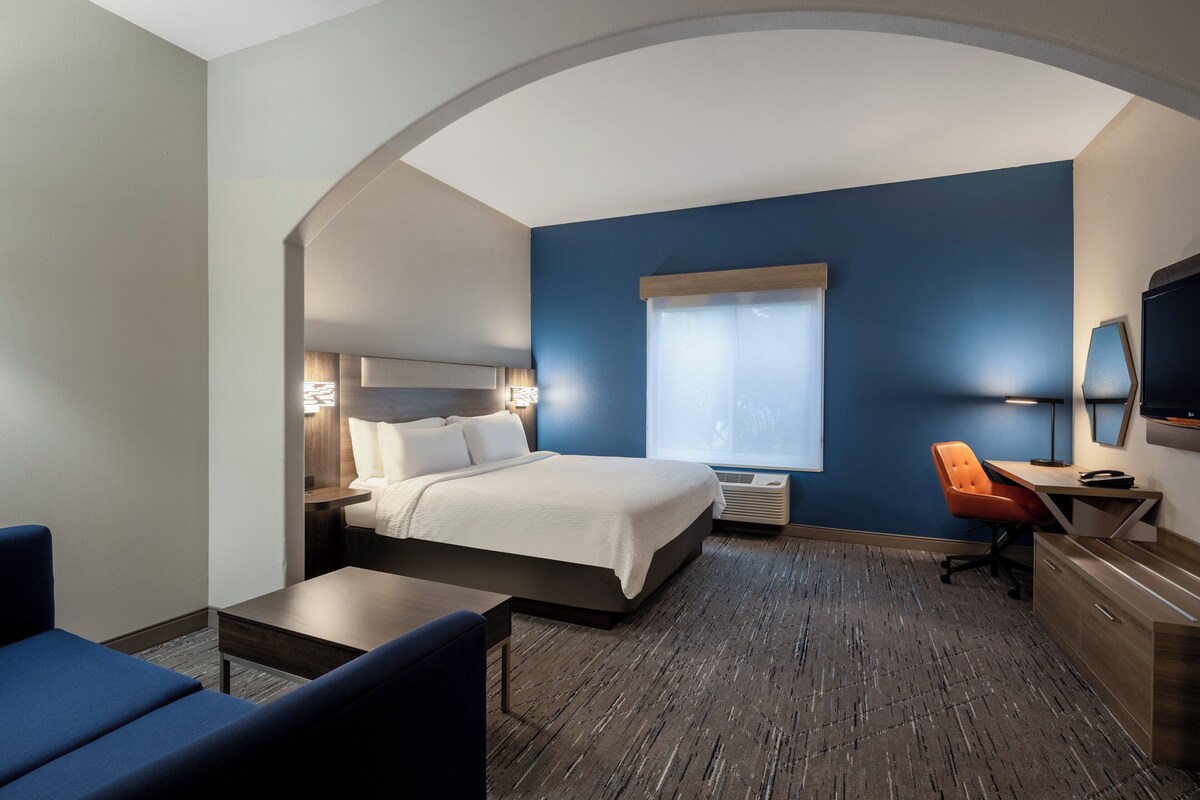A hotel room with a bed, a desk, a chair, a TV, and a window.