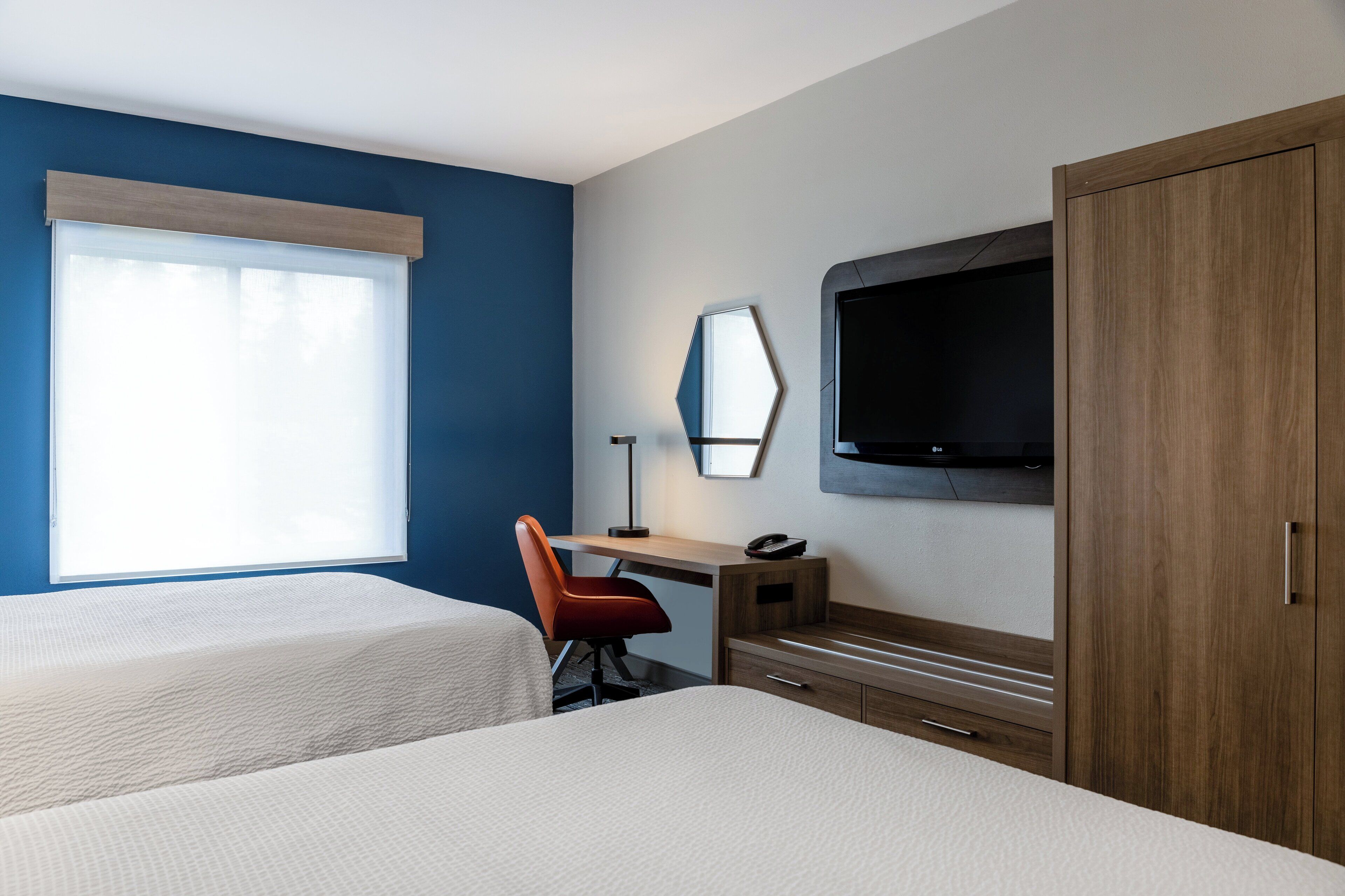 A hotel room with two beds, a desk with a chair, a TV, and a wardrobe.