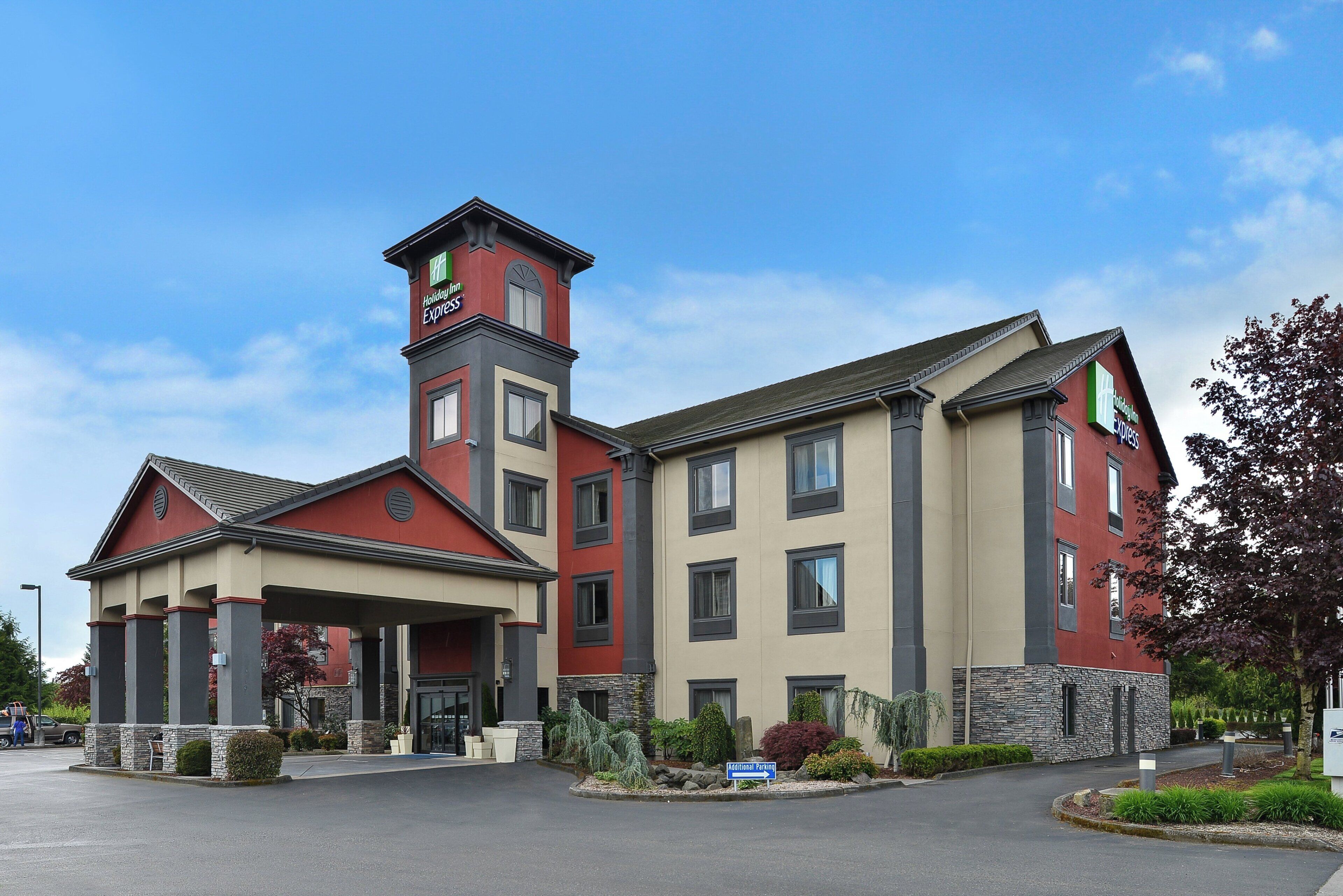 Un hotel Holiday Inn Express con una torre destacada, entrada cubierta y fachada de piedra.