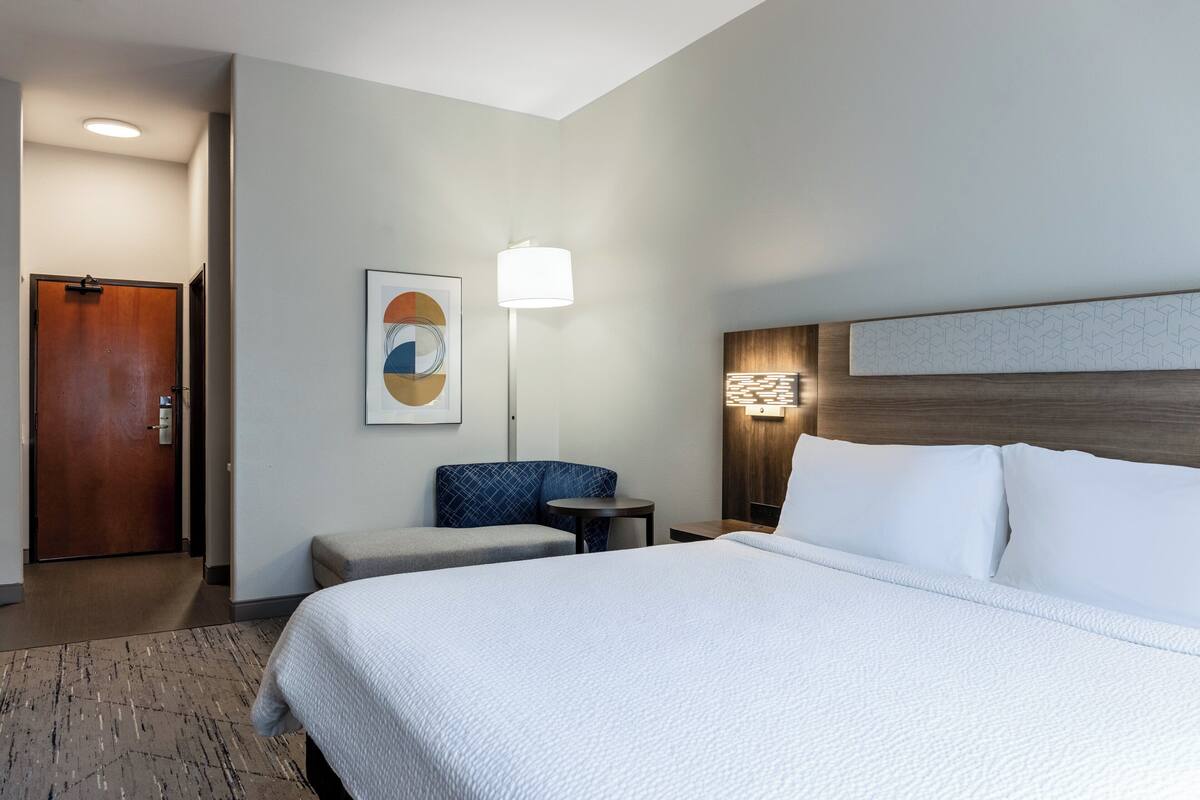 Ein Hotelzimmer mit einem großen Bett, einer Sitzecke mit Stuhl und Tisch, einer Wandlampe und einer Tür.