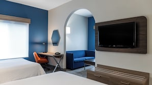 A hotel room with two beds, a desk with a chair, a TV, and a blue sofa.