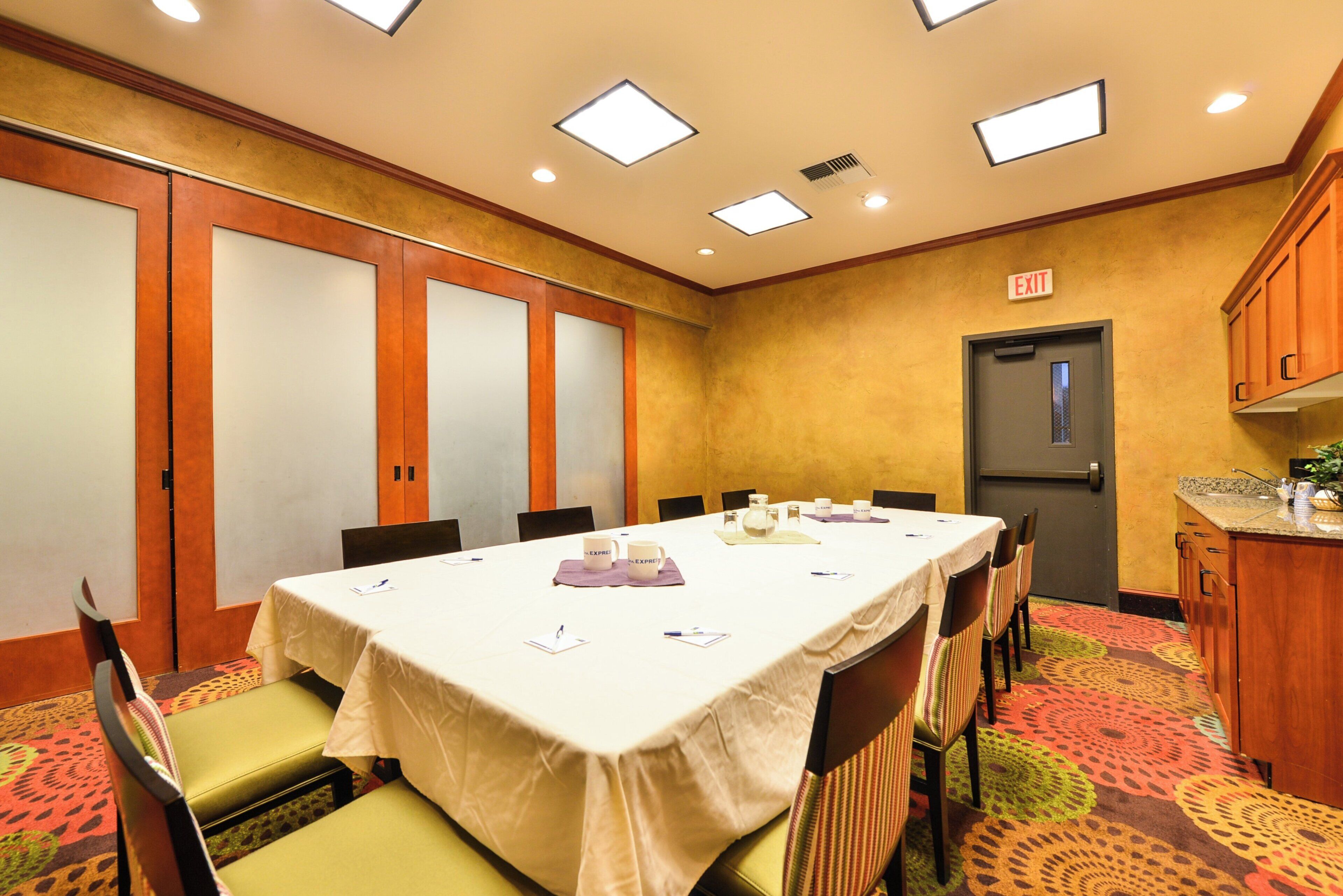 Un salón de conferencias con una larga mesa, sillas y una zona de cocina con armarios y un lavabo.