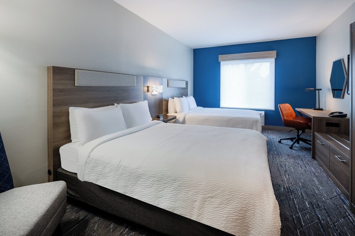 A hotel room with two beds, a desk, a chair, and a dresser.