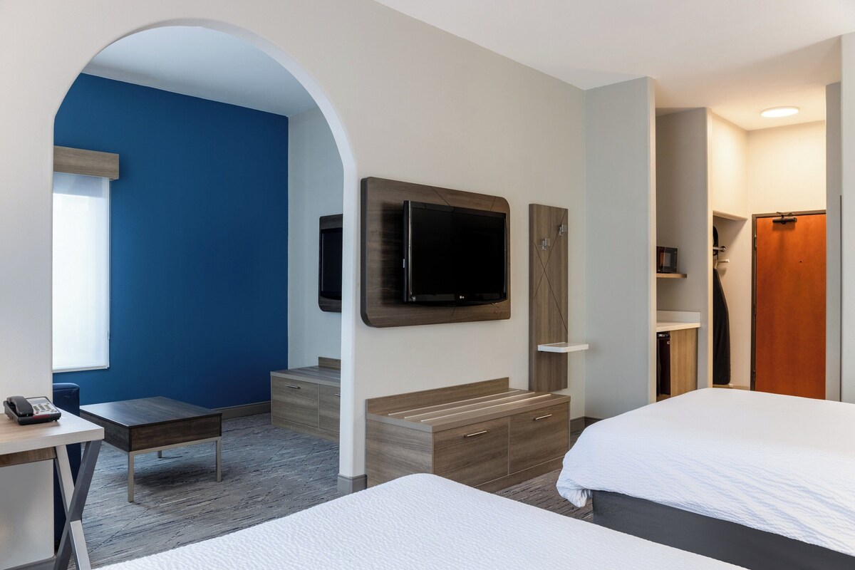 A modern hotel room with a large bed, a desk with a telephone, a TV mounted on the wall, and a wooden wardrobe.
