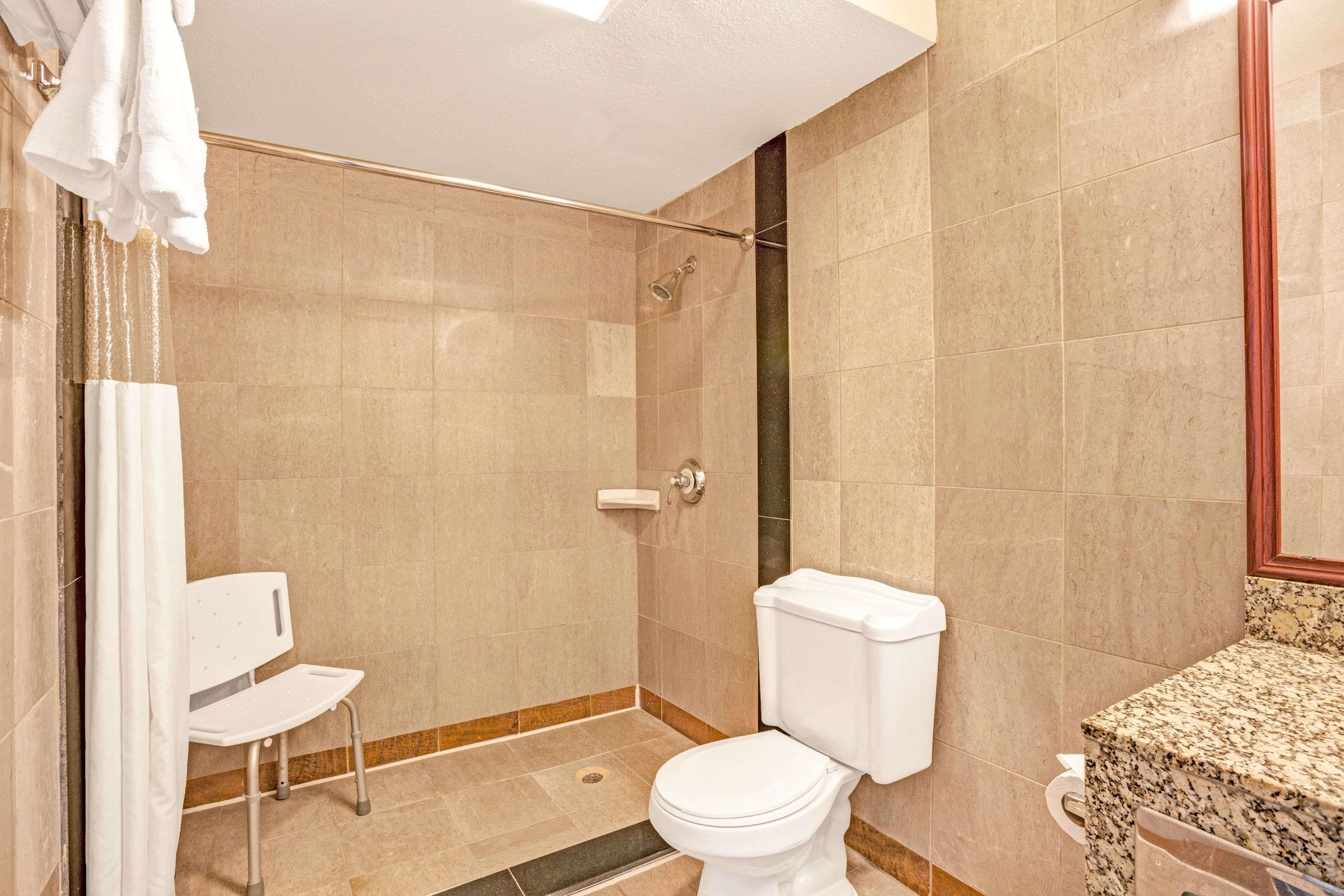A bathroom with a shower, toilet, and a chair.