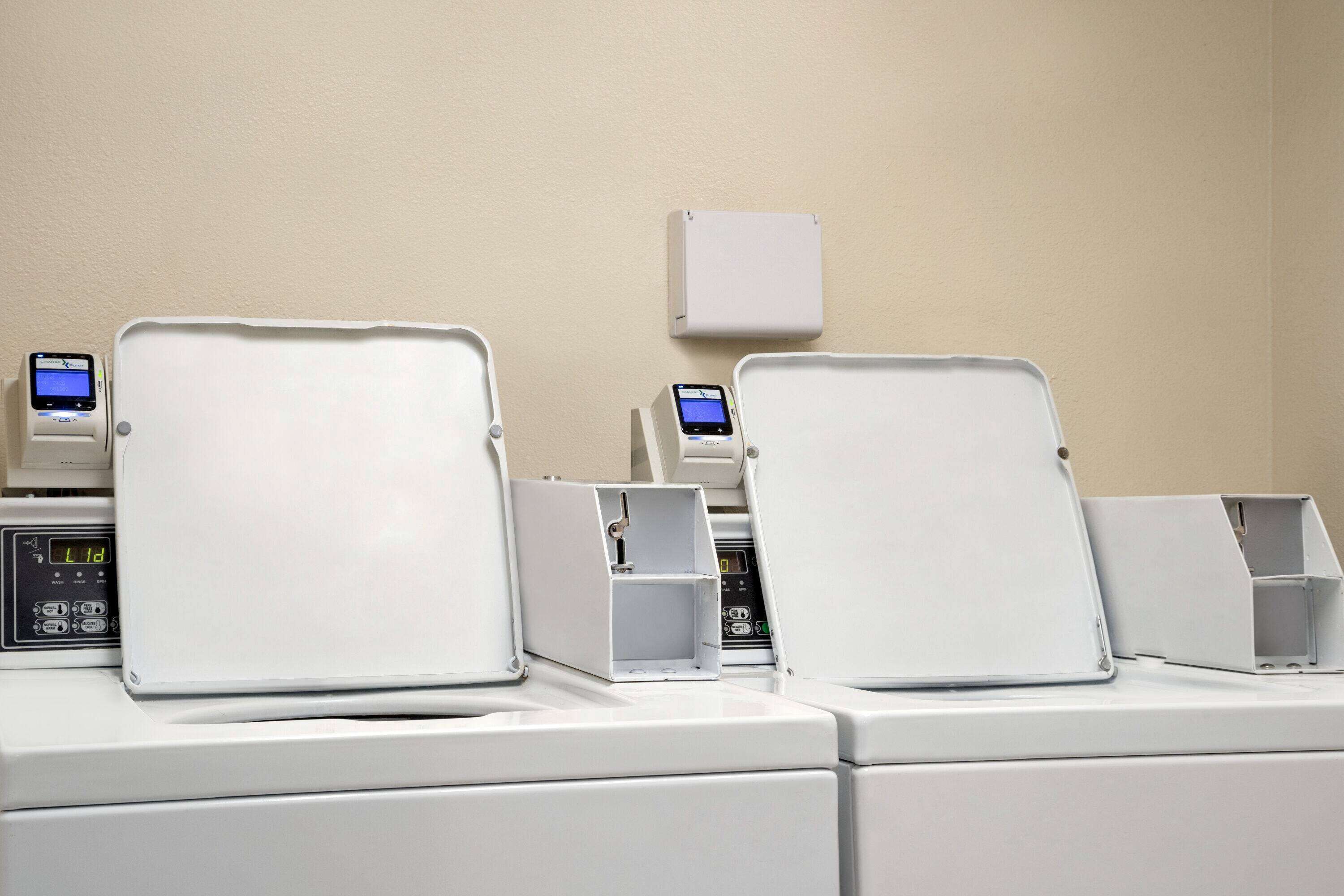 A laundry area with multiple washing machines and dryers, each with a control panel and a digital display.