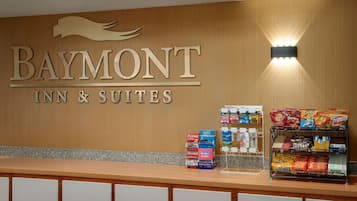 Zona de recepción de un Baymont Inn & Suites, con una pared de madera, un mostrador de recepción y una exhibición de aperitivos.