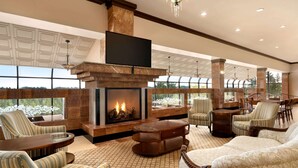 Un salón amplio con chimenea, asientos cómodos y ventanas grandes que ofrecen vistas al exterior.
