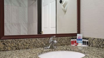 A bathroom with a granite countertop, a white sink, a mirror, and a hairdryer mounted on the wall.