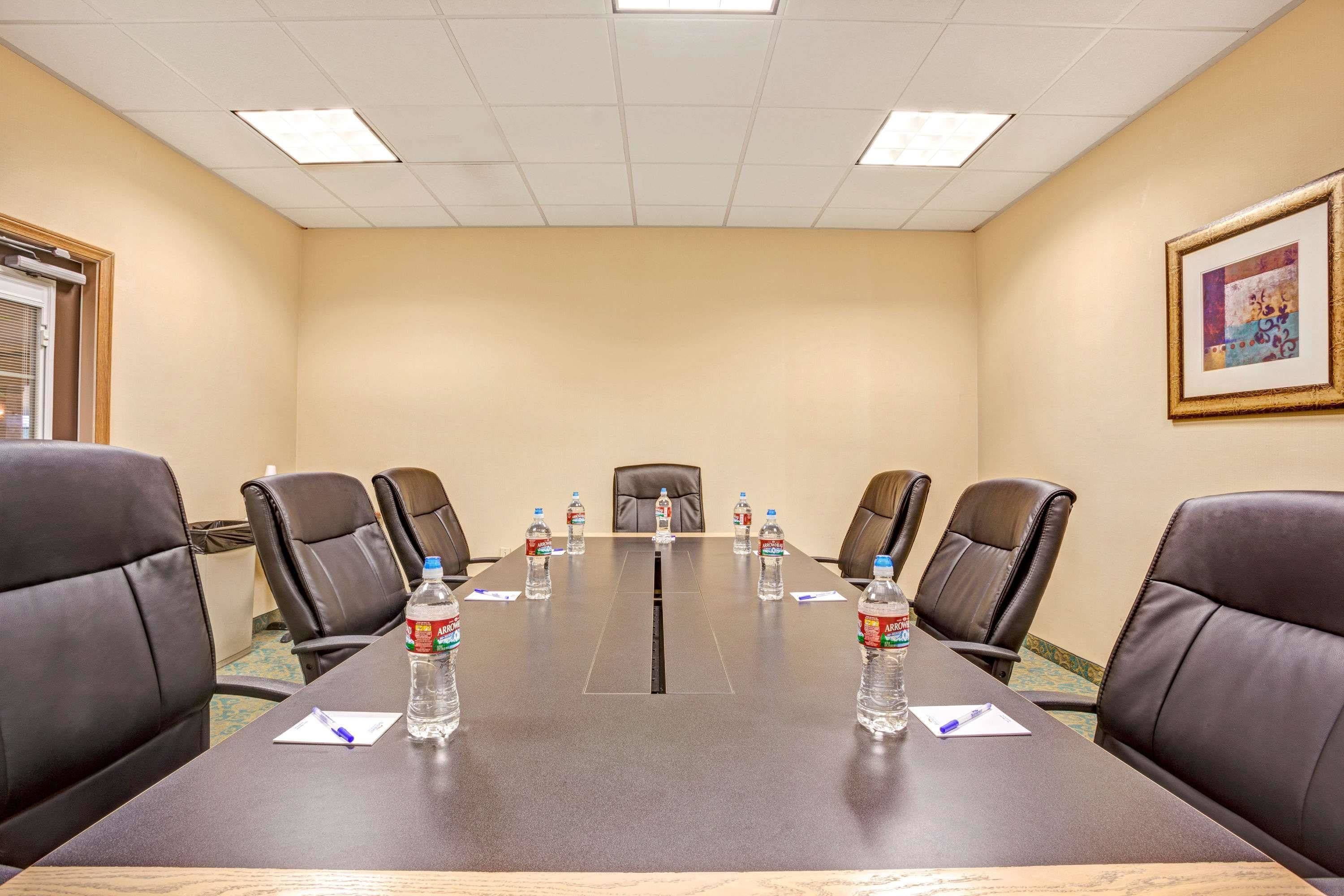 A conference room with a long table, six leather chairs, and water bottles on the table.