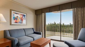 Una habitación de hotel moderna con un sofá gris, una mesa de centro de madera y vistas a un balcón con barandilla.