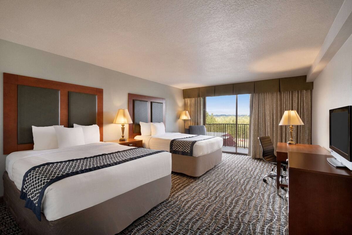 A hotel room with two beds, a desk, a chair, and a TV.