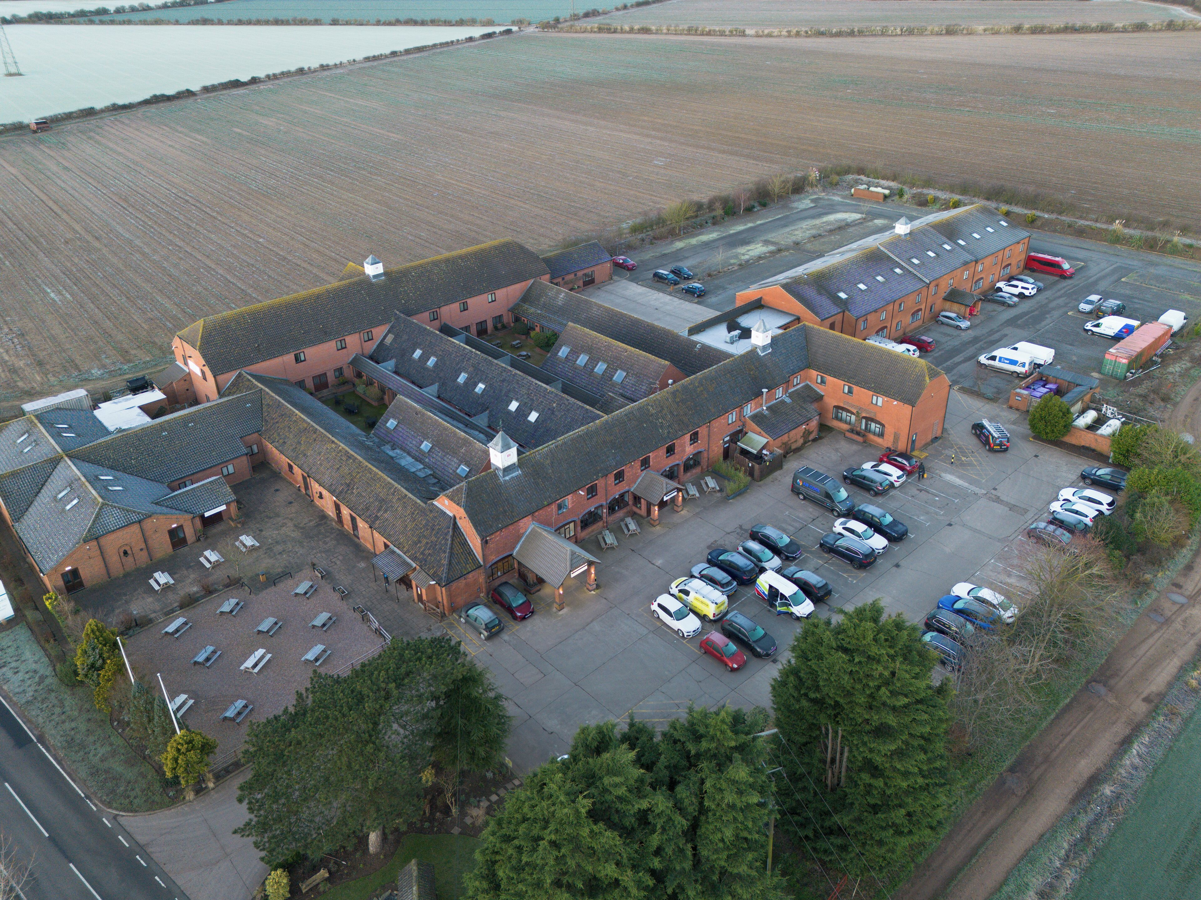 An aerial view of a building with multiple parking spaces and a large open field in the background.