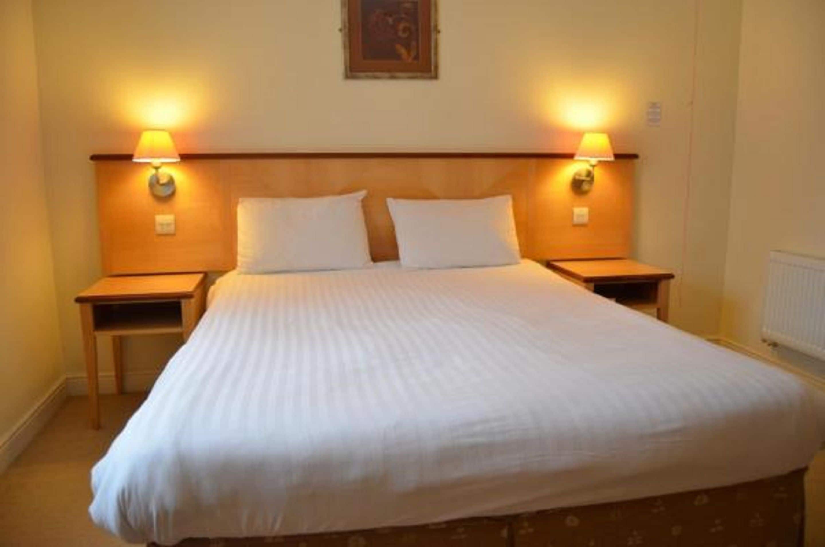 Un lit bien fait, avec deux oreillers, deux tables de chevet avec des lampes et un tableau encadré au mur.