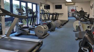 Een sportschool met loopbanden, crosstrainers en hometrainers, gerangschikt in rijen.