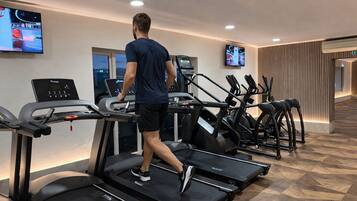 A gym with treadmills, a TV screen, and a wooden wall.