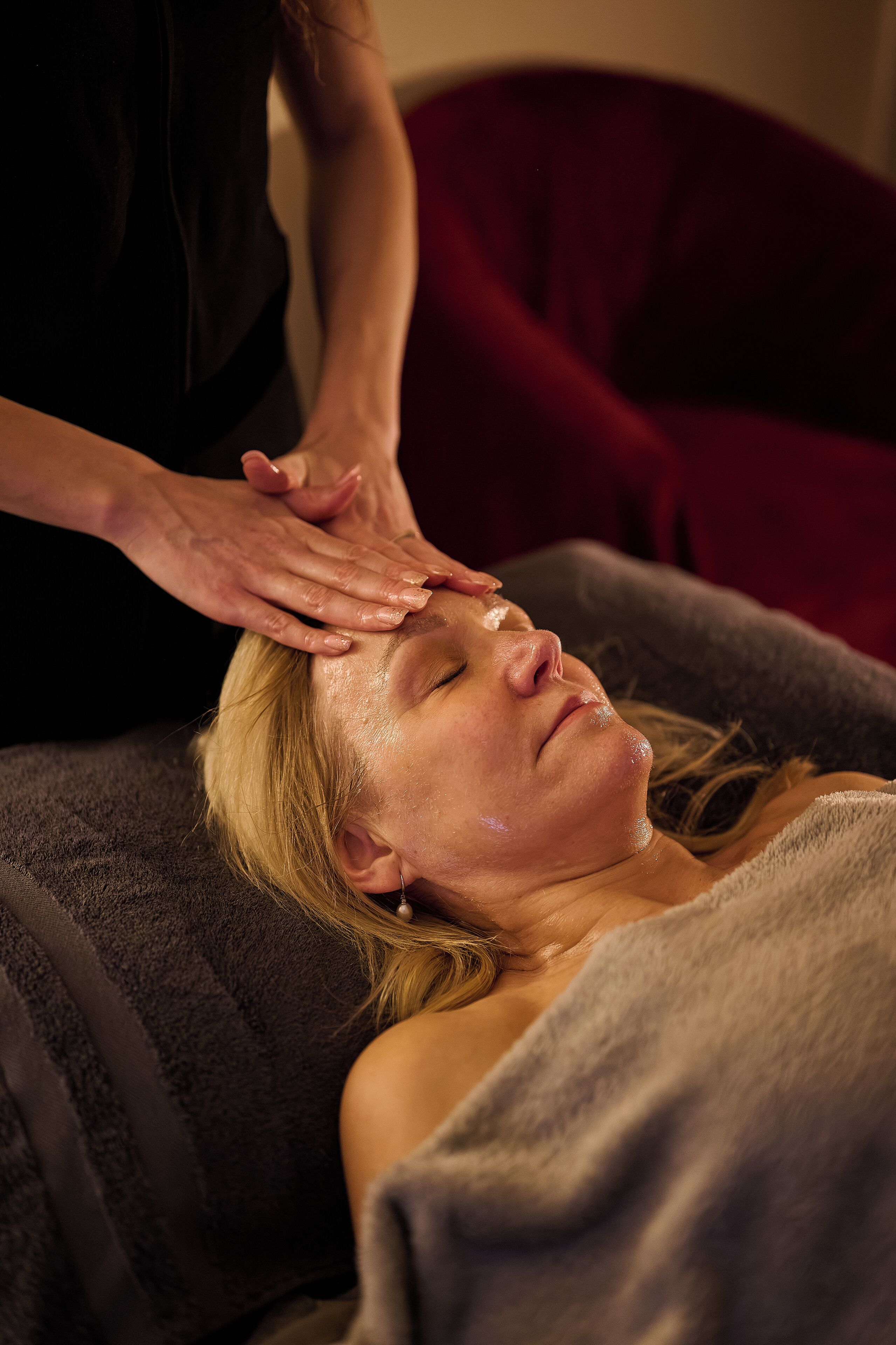 A person receiving a head massage in a room with a dark-colored headrest and a red cushion.