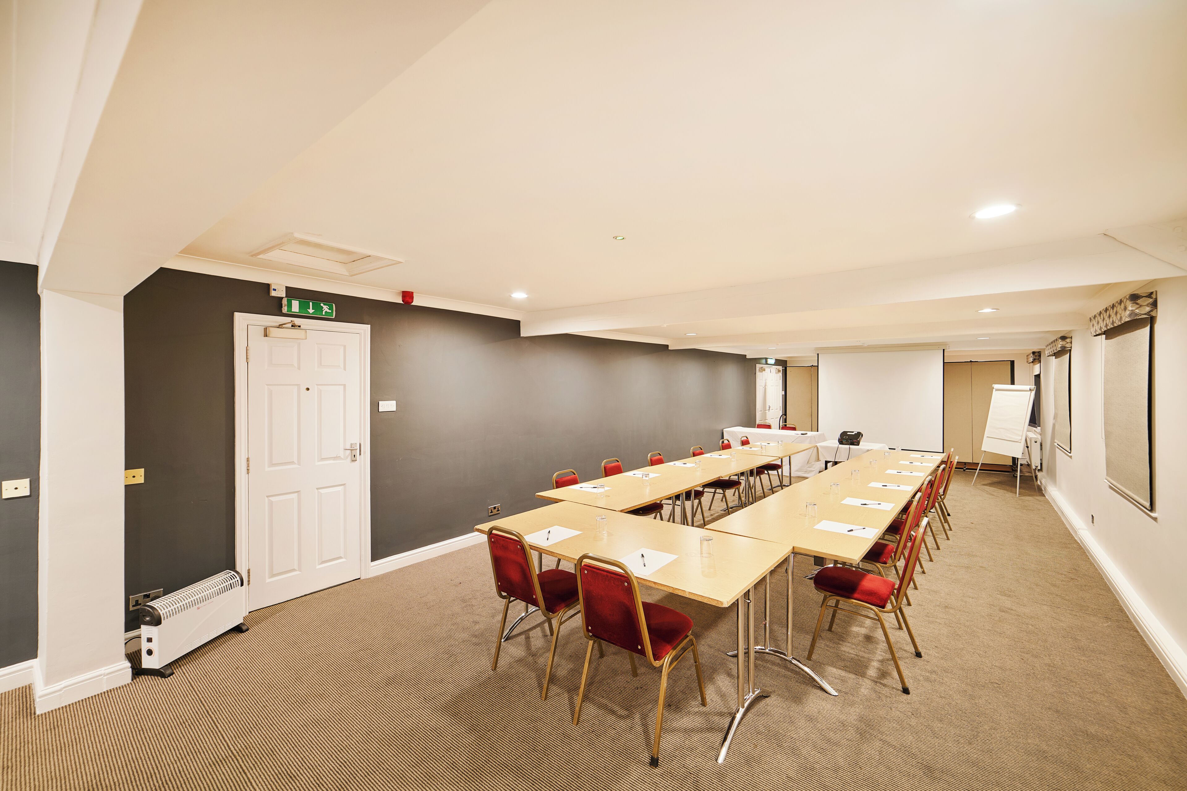 Ein Konferenzraum mit langem Tisch, roten Stühlen, einer Whiteboard und einer Projektionsfläche.