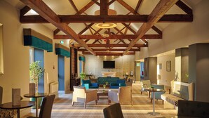 Un hall d’entrée spacieux avec de hauts plafonds, des poutres en bois, une cheminée et des coins salon confortables.